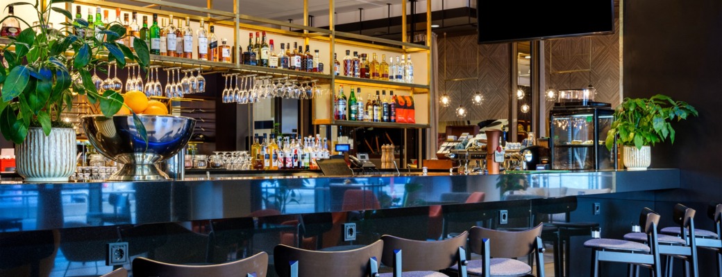 Zdjęcie hotelowego lobby baru wysokimi krzesłami, w tle butelki gatunkowych alkoholi