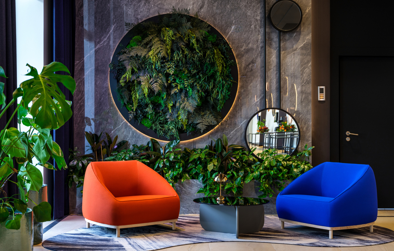 Dwa kolorowe fotele w hotelowym lobby na tle ściany z zielenią
