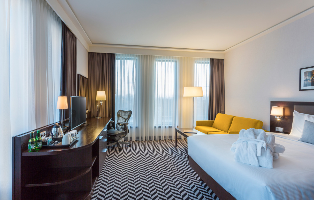 Wnętrze hotelowego pokoju z widokiem na okno, łóżko i żółtą sofę