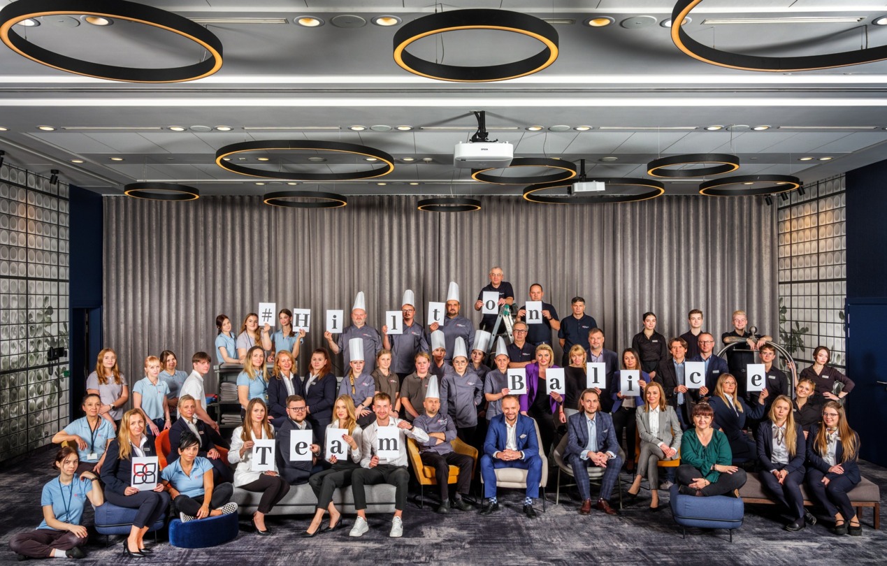 Grupowe zdjęcie pracowników hotelu trzymających w rękach napis Hilton Balice Team