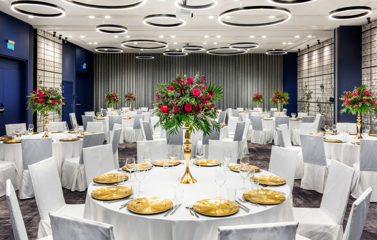 Wnętrze uroczyście zaaranżowanej sali bankietowej ze stołami, białymi obrusami i nakryciem