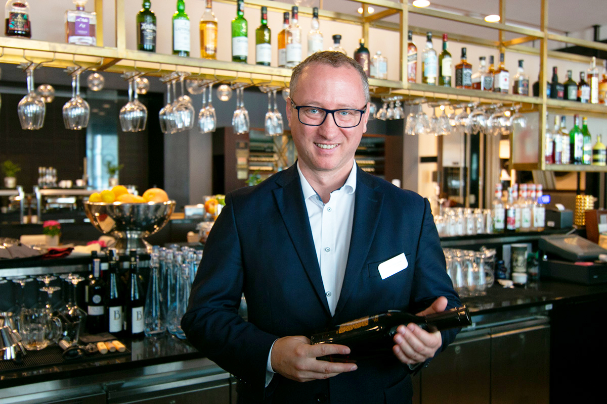 Zdjęcie kierownika restauracji z butelką wina w ręku na tle lobby baru