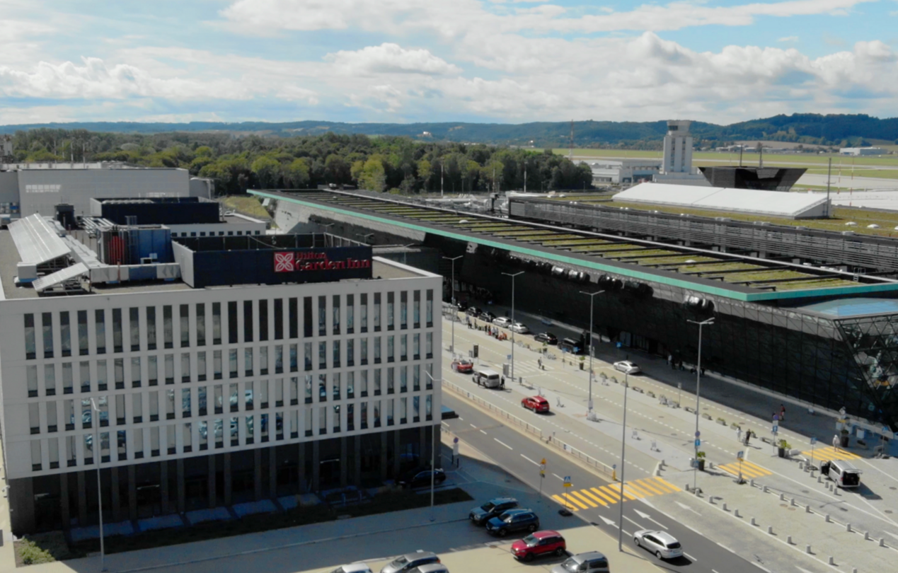 Fasada budynku hotelu widziana z lotu ptaka. W tle terminal lotniska