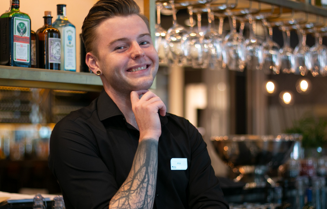 Uśmiechnięty kelner w czarnej koszuli na tle baru