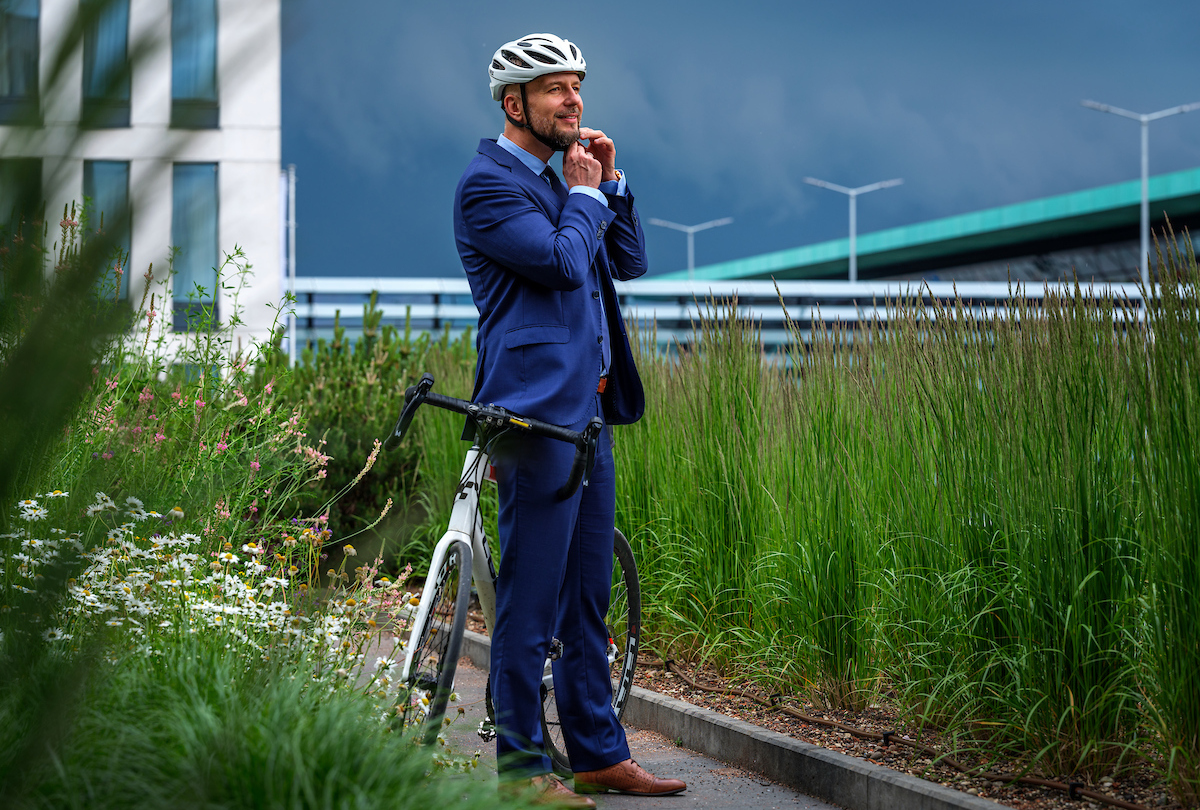 A man in a helmet and a navy blue suit poses on the roof of a hotel among the greenery, leaning on a