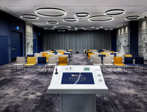 Zdjęcie sali konferencyjnej z perspektywy mównicy. W tle krzesła w ustawieniu teatralnym