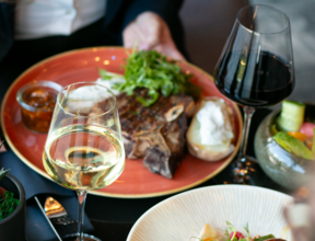 Zdjęcie stolika z dwoma daniami na kolorowych talerzach i kieliszkami wina czerwonego i białego