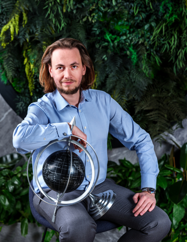 A hotel general manager sitting against a green wall holding a globe in his hand