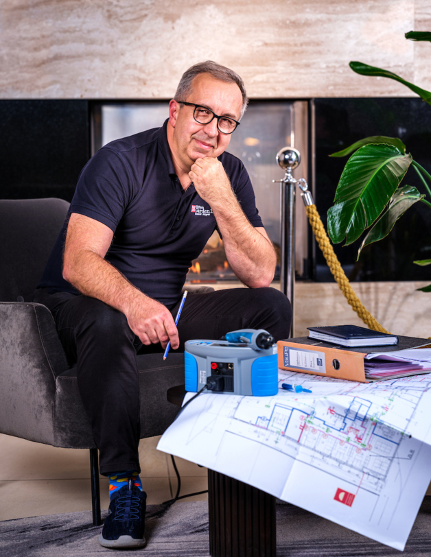A smiling man sits and leans over the architectural plans of a building