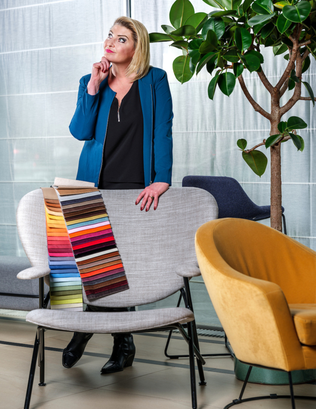 A woman in a contemplative pose leans against an armchair on which lies a fabric color sampler