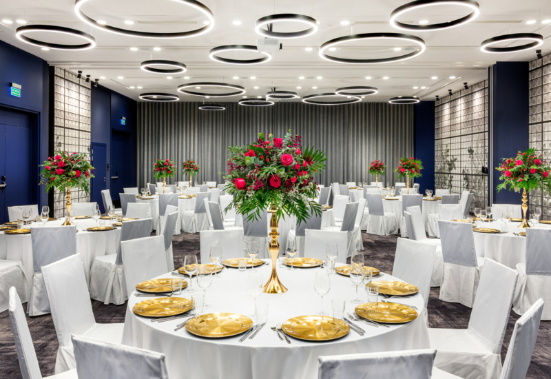 Wnętrze uroczyście zaaranżowanej sali bankietowej ze stołami, białymi obrusami i nakryciem