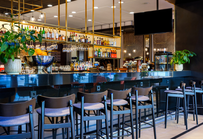 Zdjęcie hotelowego lobby baru wysokimi krzesłami, w tle butelki gatunkowych alkoholi