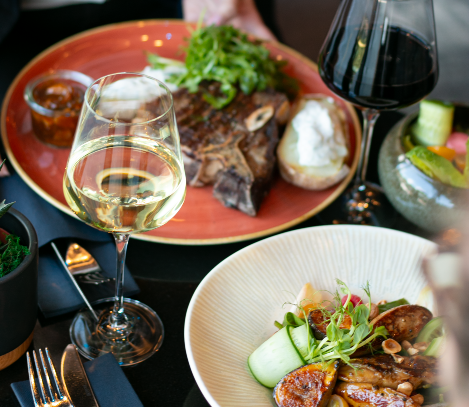 Zdjęcie stolika z dwoma daniami na kolorowych talerzach i kieliszkami wina czerwonego i białego