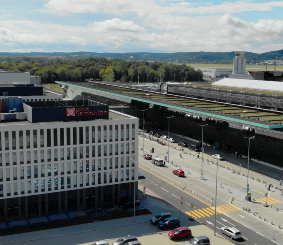 Fasada budynku hotelu widziana z lotu ptaka. W tle terminal lotniska