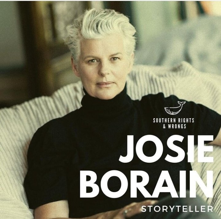 Portrait of a person with short white hair sitting on a striped cushioned chair, wearing a black turtleneck sweater