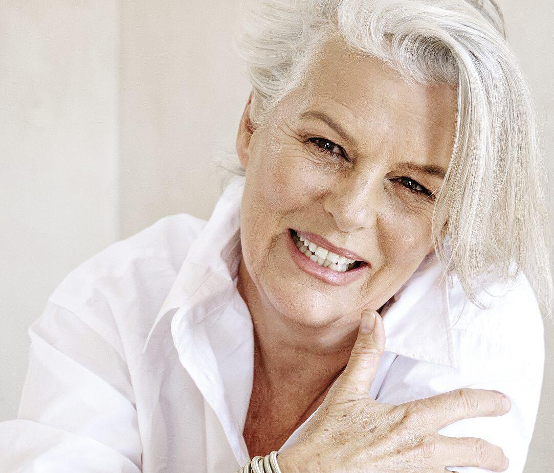 Smiling older woman with white hair wearing a white shirt and multiple silver bangles, conveying warmth and style