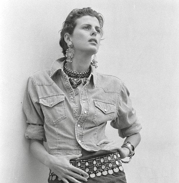 Stylish woman wearing layered necklaces, statement earrings, and a denim button-up shirt, evoking a chic, relaxed vibe.