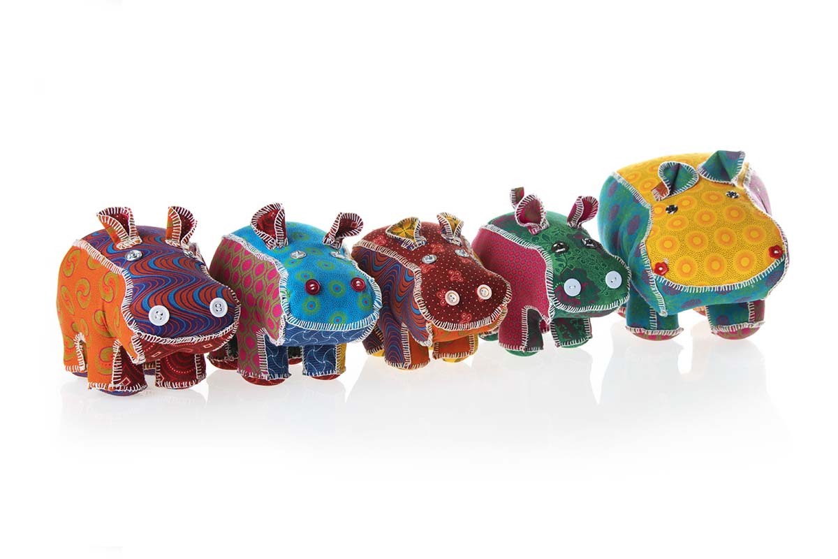 Colorful fabric hippo toys with button eyes and stitched details arranged in a row on a white background