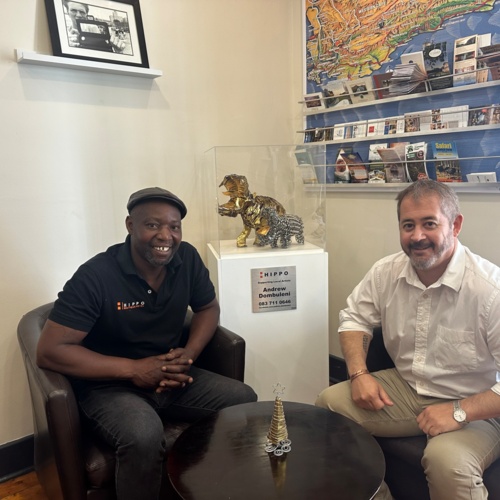Two men sitting in cozy armchairs in a hotel lobby area with local art sculptures and travel brochures on display