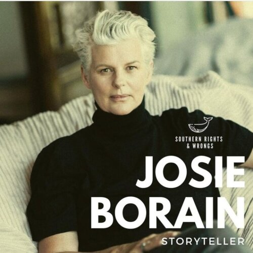 Portrait of a person with short white hair sitting on a striped cushioned chair, wearing a black turtleneck sweater