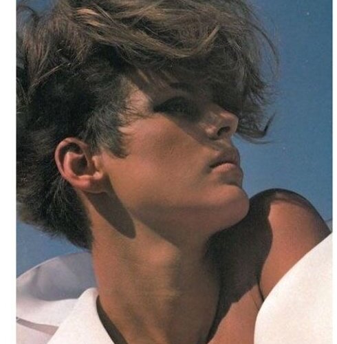 Close-up of a contemplative young person with tousled hair against a clear blue sky, wearing a white shirt collar