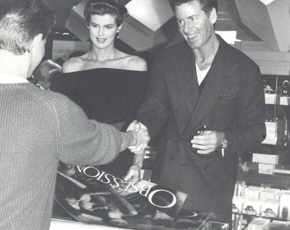 Guests interacting with a smiling man and woman at a hotel retail or gift shop counter under modern ceiling lights
