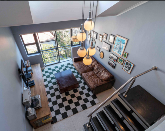 Modern loft living room with leather sofa, checkered rug, gallery wall, large windows, wood media console, and hanging globe lights