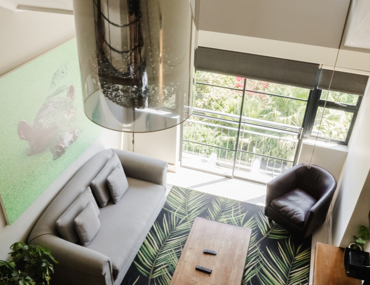 Bright loft living area with gray sofa, patterned rug, large window, leather chair, wooden coffee table, and modern décor
