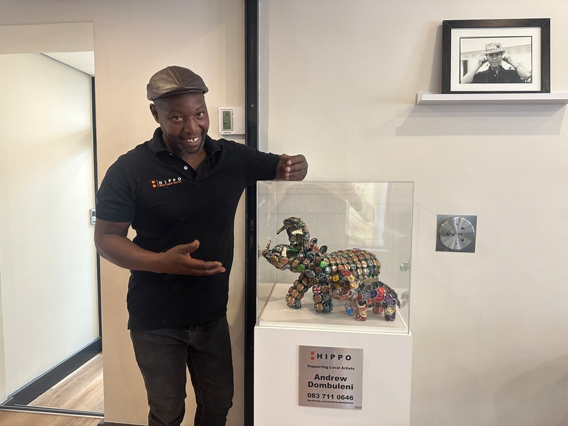 Hotel staff member in black polo presents colorful hippo sculptures made from bottle caps displayed in glass case in lobby area