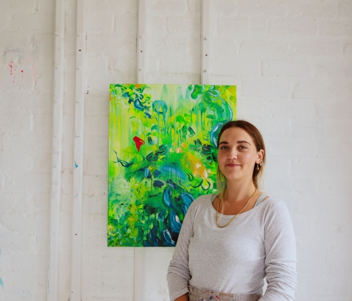 Female artist standing in bright studio with brick and white walls, colorful abstract painting, and natural light illuminating the space
