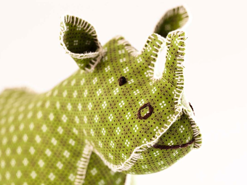 Close-up of a handmade soft fabric rhinoceros toy with green patterned fabric and stitched details