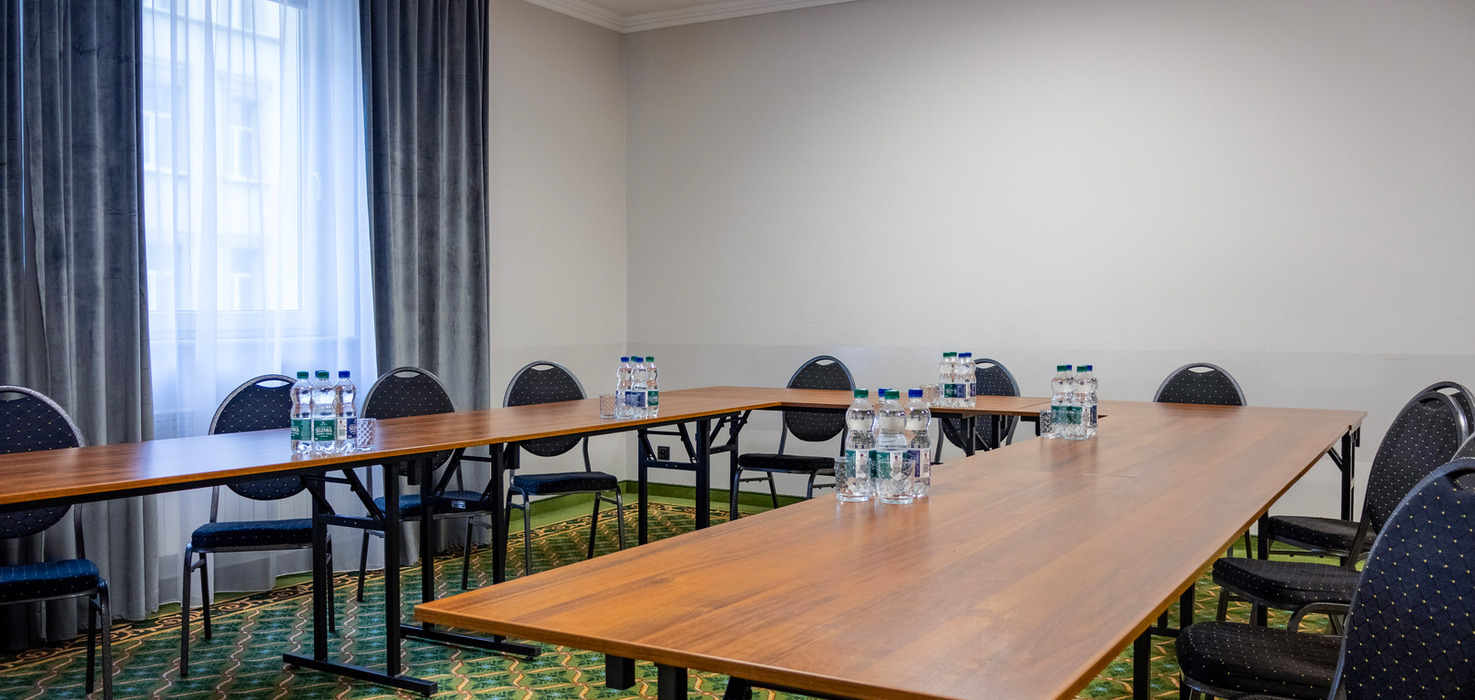 Mała sala konferencyjna hotelu z stołami w układzie U, czarnymi krzesłami, butelkami wody, projektorem i zasłoniętym oknem