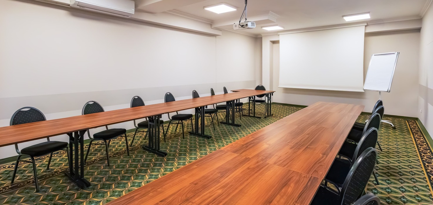 Conference room with tables in a classroom layout, a lowered projection screen, and a projector suspended from the ceiling.