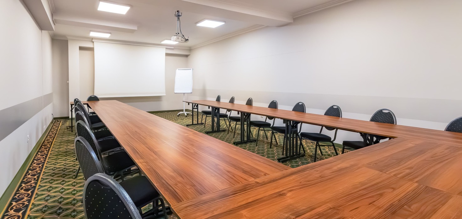 Conference room with tables in a horseshoe layout, a lowered projection screen, and a projector suspended from the ceiling.