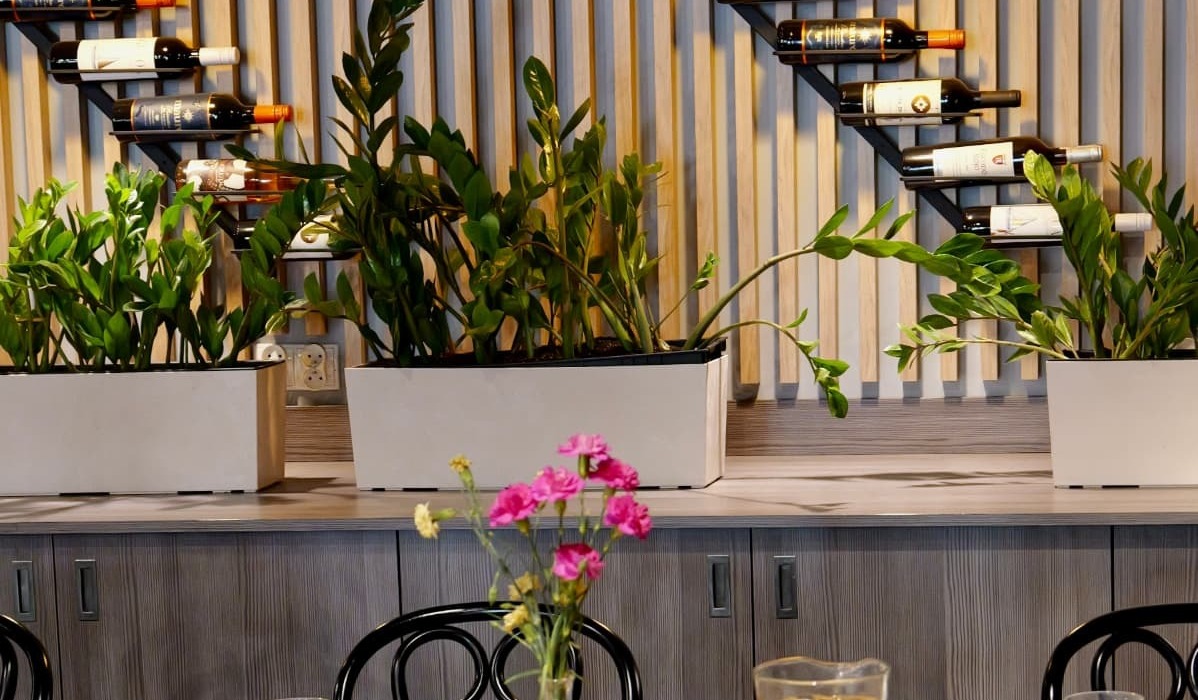 Cozy dining area with wooden tables, set place settings, pink flowers, wall wine racks and warm pendant lights