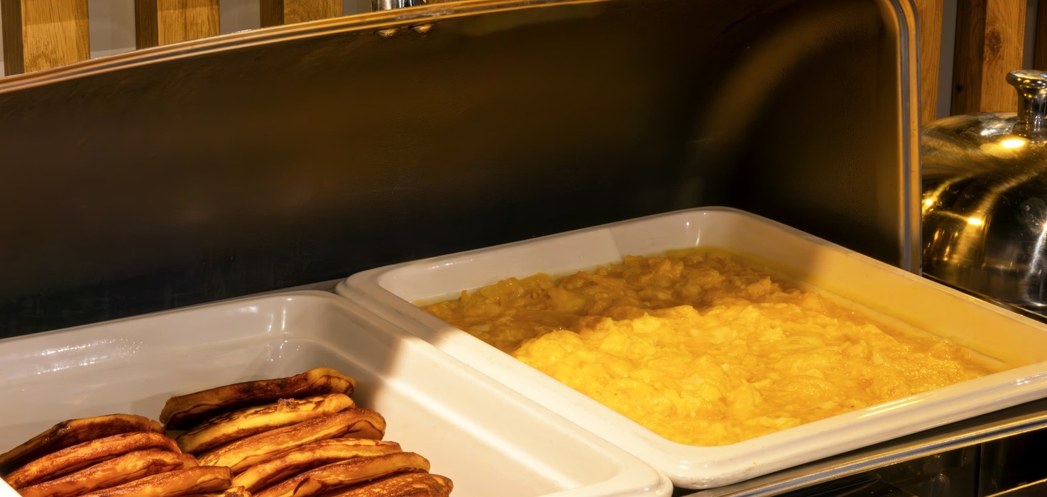 Tace śniadaniowe w bufecie hotelowym z puszystą jajecznicą i złotymi naleśnikami pod ciepłym oświetleniem.