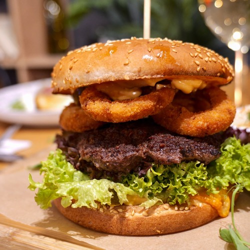Soczysty burger w sezamowej bułce z wołowym kotletem, chrupiącymi krążkami cebuli, sałatą i kubkiem ketchupu – pyszne danie w klimatycznej restauracji PragaTu w Warszawie blisko stacji metra Dworzec Wileński.