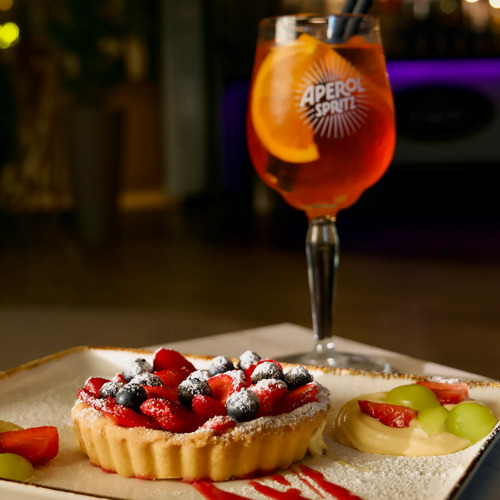Marjatarte suhkrupudriga kõrval kreemitäidisega puuviljataart, serveeritud Aperol Spritziga ja apelsiniviiluga baaris.