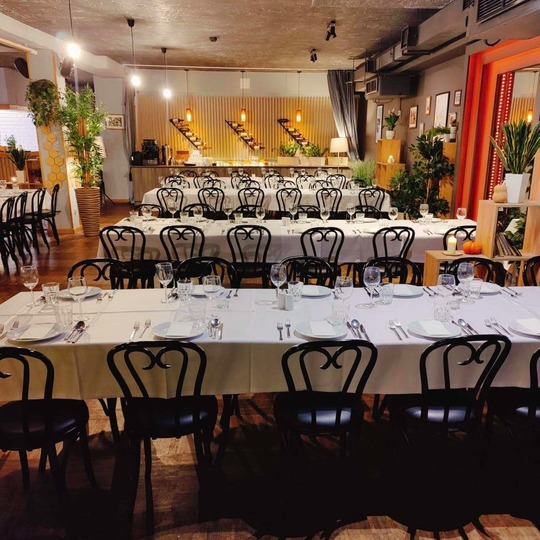 Bankettsaal mit langen, weiß gedeckten Tischen, eleganten Tischgedecken, schwarzen geschwungenen Stühlen und warmer Beleuchtung.