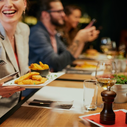 Gruppe genießt knusprige panierte Häppchen und Pommes in der lebhaften Hotel-Restaurant-Bar, lachende Gäste und Weingläser auf dem Tisch