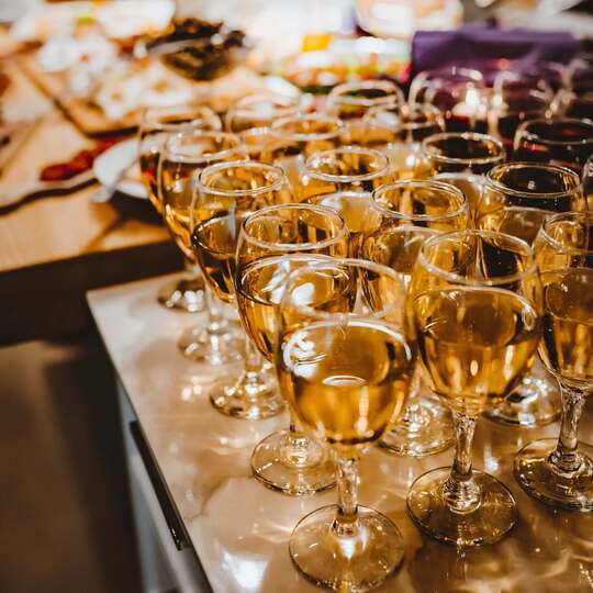 Rows of wine glasses filled with white wine on a marble buffet, warm lighting for a cocktail reception