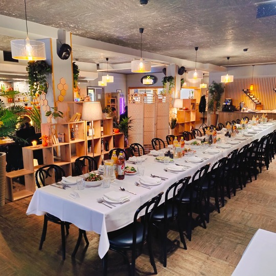 Langer Banketttisch für Hotelabendessen, weiße Tischdecken, Teller mit Vorspeisen, Flaschengetränke, warme Hängeleuchten und Holzregale.