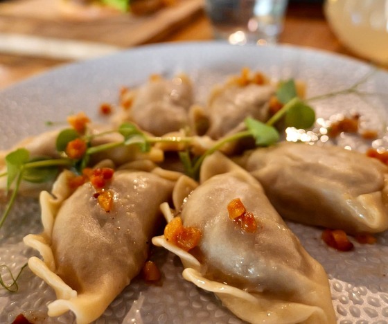 Pierogi na fakturowanym talerzu, podane z mikroliśćmi i chrupiącymi kawałkami czosnku