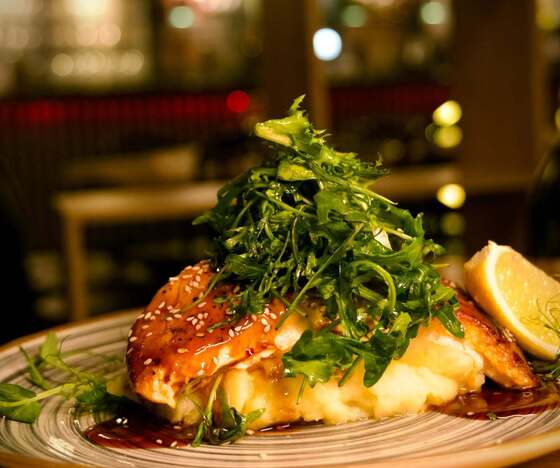 Glasierter Sesam-Lachs auf cremigem Kartoffelpüree, garniert mit Rucola und Zitronenecke im warmen Restaurant-Ambiente