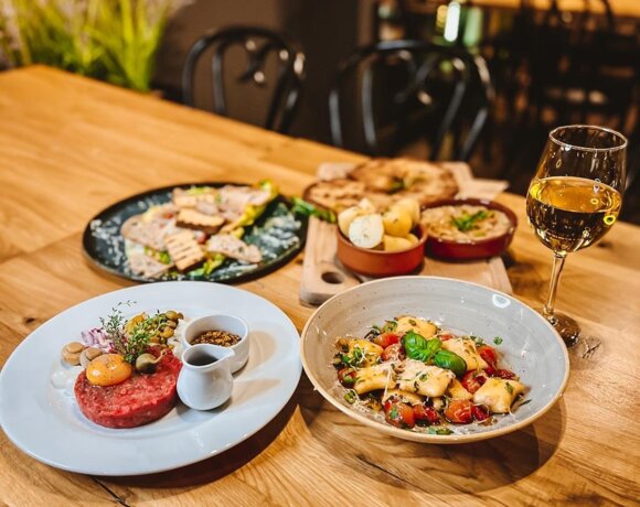 Wykwintne dania na drewnianym stole w restauracji, w tym makarony, pieczywo, puree i kieliszek białego wina.