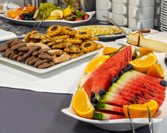 Talrza z pokrojonym arbuzem, pomarańczami i jagodami obok ciastek i kremowego ciasta na bufecie śniadaniowym hotelu.