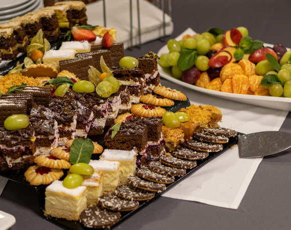 Bufet deserowy w hotelu z kawałkami ciasta czekoladowo-śmietankowego, różnorodnymi ciasteczkami, owocowymi wypiekami i półmiskiem świeżych owoców