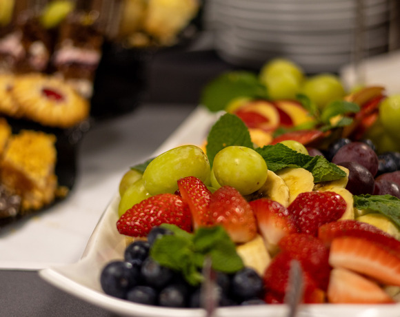 Półmisek świeżych truskawek, zielonych i czerwonych winogron, borówek, plastrów banana i mięty na bufecie hotelowym, ciastka w tle