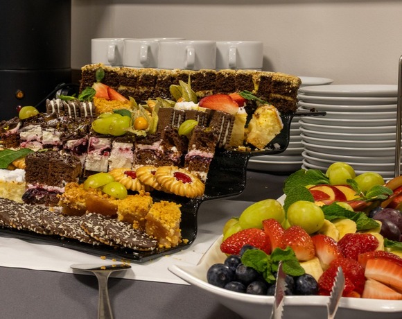 Bufetowy wybór deserów z ciastami, ciasteczkami i świeżą paterą owoców obok termosu kawy i ułożonych filiżanek