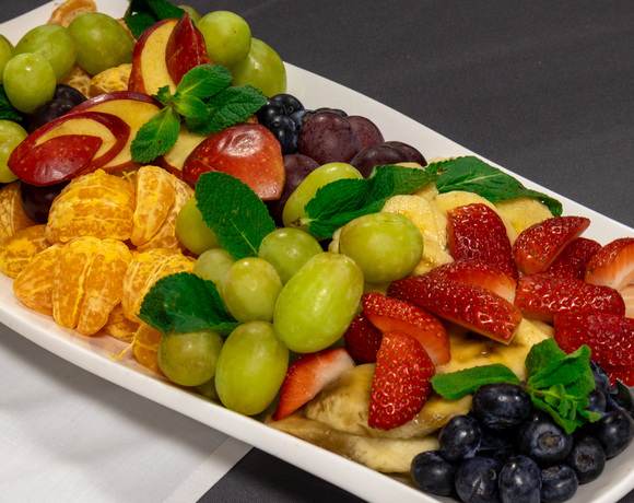 Mieszana taca świeżych owoców: truskawki, winogrona, borówki, plastry banana, kawałki mandarynki i mięta — śniadanie w hotelu